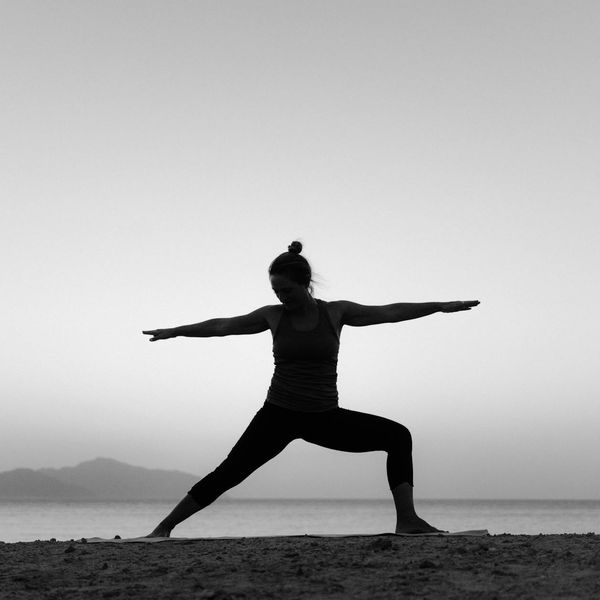 Woman holding a strong warrior yoga pose outdoors at sunset.